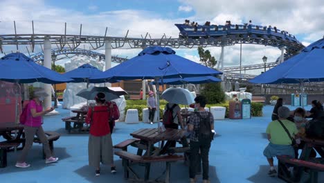 Los-Visitantes-Comen-Durante-La-Hora-Del-Almuerzo-Mientras-La-Montaña-Rusa-Artic-Blast-Pasa-Por-Encima-De-Ellos-En-El-Parque-Temático-De-Diversiones-Y-Animales-Ocean-Park-En-Hong-Kong