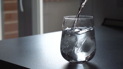 Verter-Agua-Dentro-De-Un-Vaso-Transparente-Con-Cubitos-De-Hielo-Bebida-Refrescante-Fría,-Primer-Plano-Todavía-Tiro