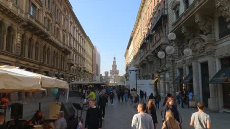 Important-Via-Dante-pedestrian-street-in-Milan-with-people-strolling-and-shopping-with-Sforza-Castle-in-background,-Italy