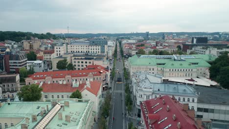 AERIAL:-Flying-Over-Gediminas-Avenue-in-Summer-on-Blue-Hour-Time-with-People-Walking-and-Vehicles-Driving-in-Streets