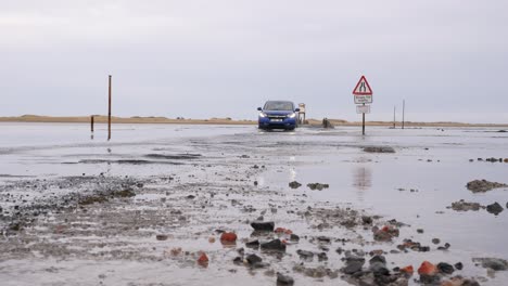 Auto-Fährt-Durch-Salzwasser-Entlang-Des-Damms-Von-Holy-Island,-Northumberland