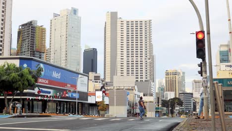 Eine-Frau-Mit-Einer-Maske-Im-Gesicht-Geht-über-Einen-Fußgängerüberweg,-Mit-Blick-Auf-Die-Stadt-Und-Die-Hohen-Wolkenkratzer-In-Obarrio,-Via-España,-Panama