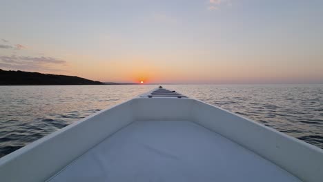 Bow-of-boat-moving-forward-over-sea-water-pointing-toward-golden-sunset-in-background
