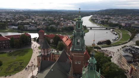 Aerial-view-of-the-Vistula-River-and-the-Wawel-Royal-Castle,-the-cathedral-and-a-courtyard-with-walking-people-in-the-foreground