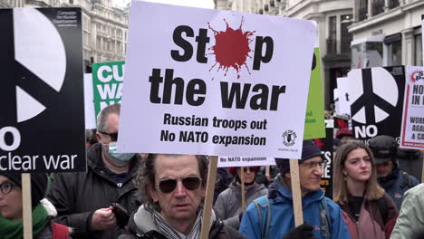 A-slow-motion-shot-of-people-stood-holding-various-anti-war-placards-on-a-Stop-The-War-Coalition,-protest-opposing-the-Russian-invasion-of-Ukraine