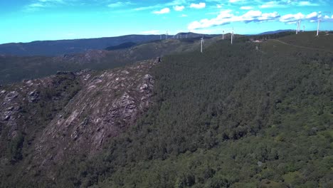 Aerial-View-Of-Rocky-Mountain-Hillside-In-Esteiro,-Spain-With-Turbines-Seen-In-Distance