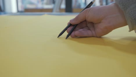 Artist-sketching-using-two-pencils-on-yellow-paper