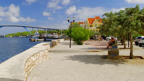 Hermoso-Paseo-Marítimo-En-Punda,-Willemstad,-En-La-Isla-Caribeña-De-Curacao-Con-El-Puente-De-La-Reina-Juliana-Al-Fondo