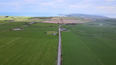 Vuelo-Recto-Hacia-Atrás-Sobre-La-Carretera-Rural-Cerca-De-Kinsale-Con-Vistas-A-Los-Campos-Verdes-Y-Nubes-Distantes-Sobre-El-Océano