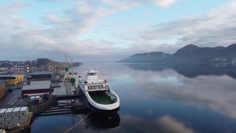 LNG-powered-car-ferry-Bergensfjord-from-Fjord1-company-is-alongside-in-Sandnes-city-for-repairs---Upward-moving-morning-aerial-with-beautiful-sky-and-reflections-in-sea---Norway