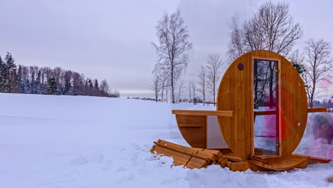 People-building-wooden-barrel-thermowood-sauna-in-snowy-country,-timelapse