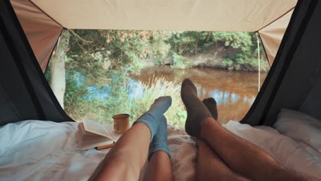 Füße-Eines-Paares-In-Einem-Zelt,-Das-Während-Eines-Campingausflugs-Auf-Einen-Wasserfluss-Blickt