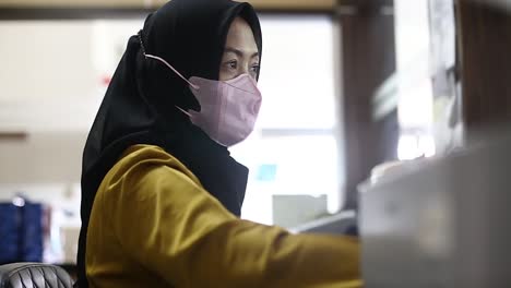 Eine-Junge-Frau-Mit-Hijab-Oder-Kopftuch-Arbeitet-Drinnen-Und-Trägt-Eine-Schützende-Medizinische-Gesichtsmaske-Für-Das-Corona-Virus