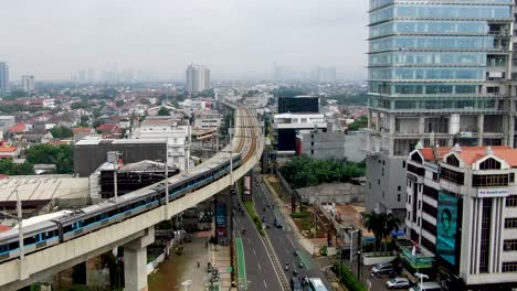 MRT-trains-on-tracks-over-roads-and-skyline-of-Jakarta,-forward-aerial