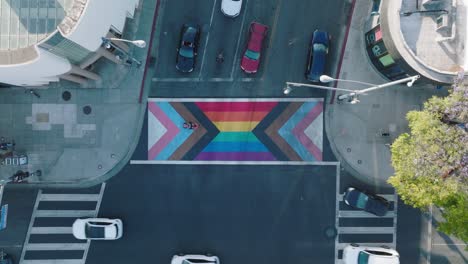 Aerial-Footage-Over-Colorful-Rainbow-Patterned-Intersection,-Cars-Turning-and-Pedestrians-Walking