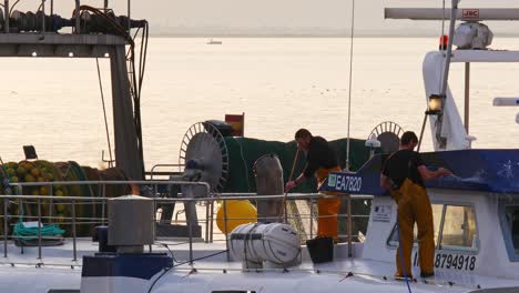 Zwei-Seearbeiter-Waschen-Bei-Sonnenuntergang-Das-Deck-Eines-Fischereifahrzeugs