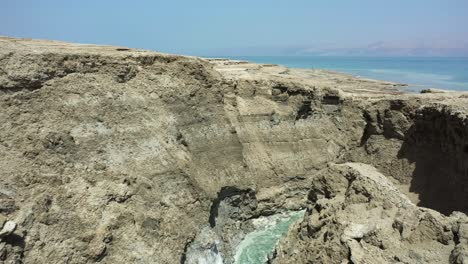 Dead-Sea-Hot-Springs-aerial-slow-fly-in-through-and-above-desert-canyon-landscape-with-crystal-clear-warm-waters-flowing-down-to-sea