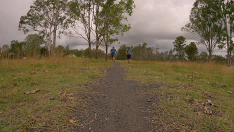 Dos-Excursionistas-Masculinos-Caminando-Desde-La-Distancia,-Hacia-La-Cámara,-A-Lo-Largo-De-Un-Camino-De-Grava,-Sendero-Ferroviario-Del-Valle-De-Brisbane,-Qld-4k