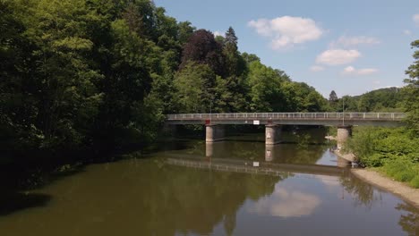 Ein-Auto-überquert-Eine-Schmale-Brücke,-Die-Sich-Perfekt-Im-Flachen-Braunen-Flusswasser-Darunter-Spiegelt