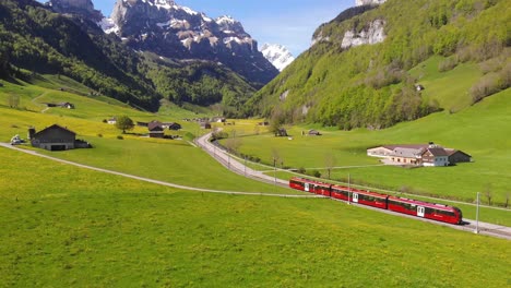 Aerial-footage-of-a-train-passing-through-snow-capped-mountain-in-Switzerland-on-a-sunny-day