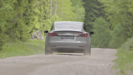 Lente-Larga-Trasera:-Un-Tesla-Model-3-2020-Conduce-Por-Un-Camino-De-Tierra-Boscoso
