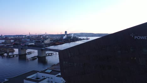 Am-Späten-Abend-über-Dem-Energie-Plus-Haus-Kraftwerk-In-Porsgrunn-Norwegen-Fliegen-–-Logo-Auf-Dem-Haus-Sichtbar-Und-Stadtbrücke-Mit-Kanal-Und-Heroya-Industriegebiet-Im-Hintergrund