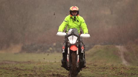 Off-road-motorcycle-driver-in-fluorescent-flame-retardant-clothing-skids-in-deep-mud-in-adventure-trial,-Slow-Motion-mud-ripping-through-rainy-autumn-wild-thick-afternoon-brown-forest