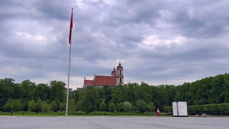 Bandera-Lituana-Colgada-En-Un-Asta-De-Bandera-Y-Un-Niño-Corriendo-En-La-Plaza-Lukiskes-En-Vilnius,-Lituania