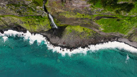 Bride's-Veil-falls-from-vertical-cliffside-onto-rocky-coastline,-Madeira