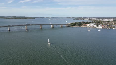 Aerial-view-around-a-sailboat,-sailing-in-front-of-the-bridge,-summer-morning-in-Taren-Point,-Sydney
