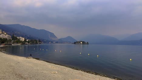 Lakeshore-of-Lake-Maggiore-with-hotels-and-Alps-mountain-range-in-background-on-cloudy-day,-Stresa-in-Italy