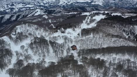Kleine-Hütte-In-Den-Berghügeln-Im-Winter-Mit-Schnee-Bedeckt-Im-Nozawa-Onsen-Japan,-Luftaufnahme