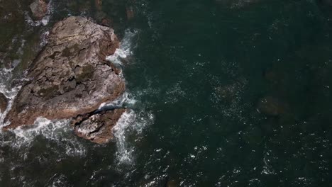 top-view-down-of-the-deep-green-water-of-the-pacific-ocean-beating-the-rocks-of-the-shoreline