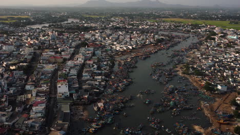 Boats-in-busy-fishing-port-on-Song-Dinh-river-in-La-Gi-town,-Vietnam,-aerial-view