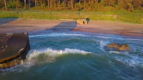 Aerial-view-of-abandoned-seaside-fortification-buildings-at-Karosta-Northern-Forts-on-the-beach-of-Baltic-sea-,-waves-splash,-golden-hour-sunset,-wide-drone-dolly-shot-moving-left