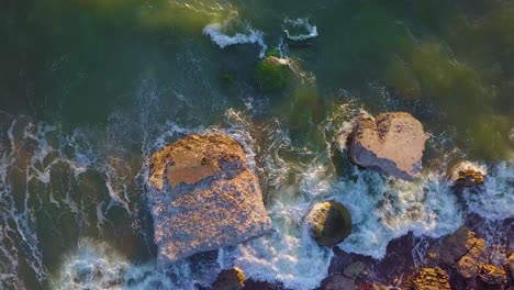 Aerial-birdseye-view-of-abandoned-seaside-fortification-buildings-at-Karosta-Northern-Forts-on-the-beach-of-Baltic-sea-,-waves-splash,-golden-hour-sunset,-wide-static-drone-shot