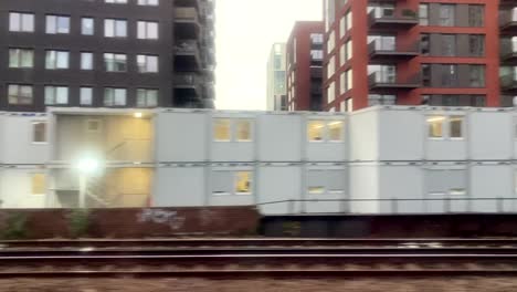 Blick-Aus-Dem-Fenster-Eines-Zuges,-Der-Mit-Der-Eisenbahn-In-Einer-Modernen,-Geschäftigen-Stadt-Fährt