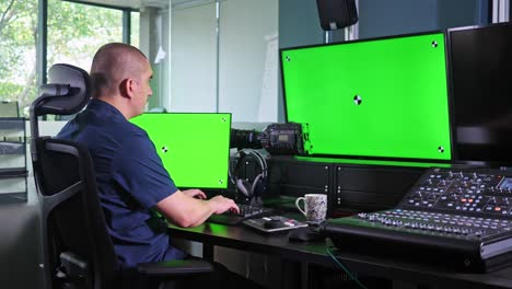Male-video-editor-works-with-software-on-chroma-screens-then-stands-up