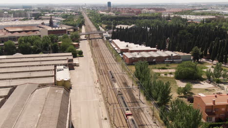 Passenger-train-driving-through-suburbs-of-Madrid,-aerial-drone-view