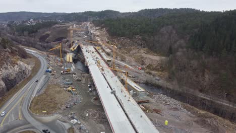 Construction-of-new-high-speed-highway-E39-between-Mandal-and-Kristiansand-in-southern-Norway---Aerial-flying-above-bridge-construction-site-at-Bringeheia-and-Klepland-with-soegneelva-river-below