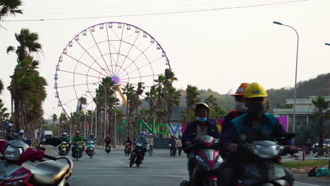 Bikers-riding-on-street-of-Phan-thiet,-amusement-park-in-background,-Vietnam