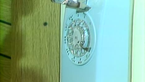 Frauenhände-Nehmen-Ein-Altes-Telefon-Mit-Wählscheibe-In-Die-Hand-Und-Hängen-Es-Auf,-1983