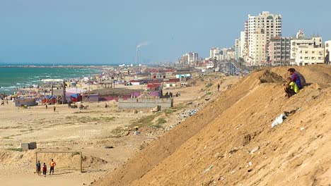 Three-people-sitting-on-the-side-of-a-tall-sand-bank-on-the-coast-of-the-Gaza-Strip,-Palestine