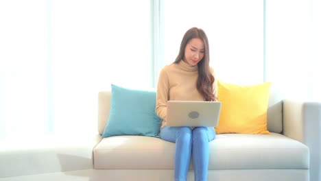 Asiatisches-Mädchen-Mit-Computer-Sitzt-Zu-Hause-Auf-Dem-Sofa