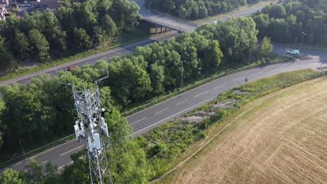 5G-broadcasting-tower-antenna-aerial-tilt-up-to-British-countryside-with-vehicles-travelling-on-highway-background