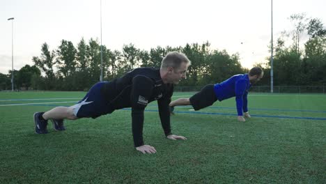 Two-men-doing-push-ups-on-a-soccer-field-early-in-the-morning