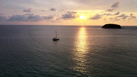 Luftflug-über-Ruhigem-Wasser-Bei-Sonnenuntergang-Mit-Nach-Oben-Geneigtem-Blick-Auf-Die-Silhouette-Einer-Schwimmenden-Yacht-Mit-Der-Insel-Im-Hintergrund