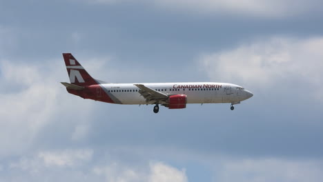 Canadian-North-Boeing-737-aircraft-descending-with-wheels-down-landing-against-blue-cloud-sky