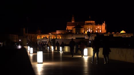 People-walking-over-famous-roman-bridge-in-Cordoba,-Spain-at-night