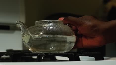 Front-view-of-an-African-American-man-taking-a-boiling-glass-tea-pot-off-the-stove